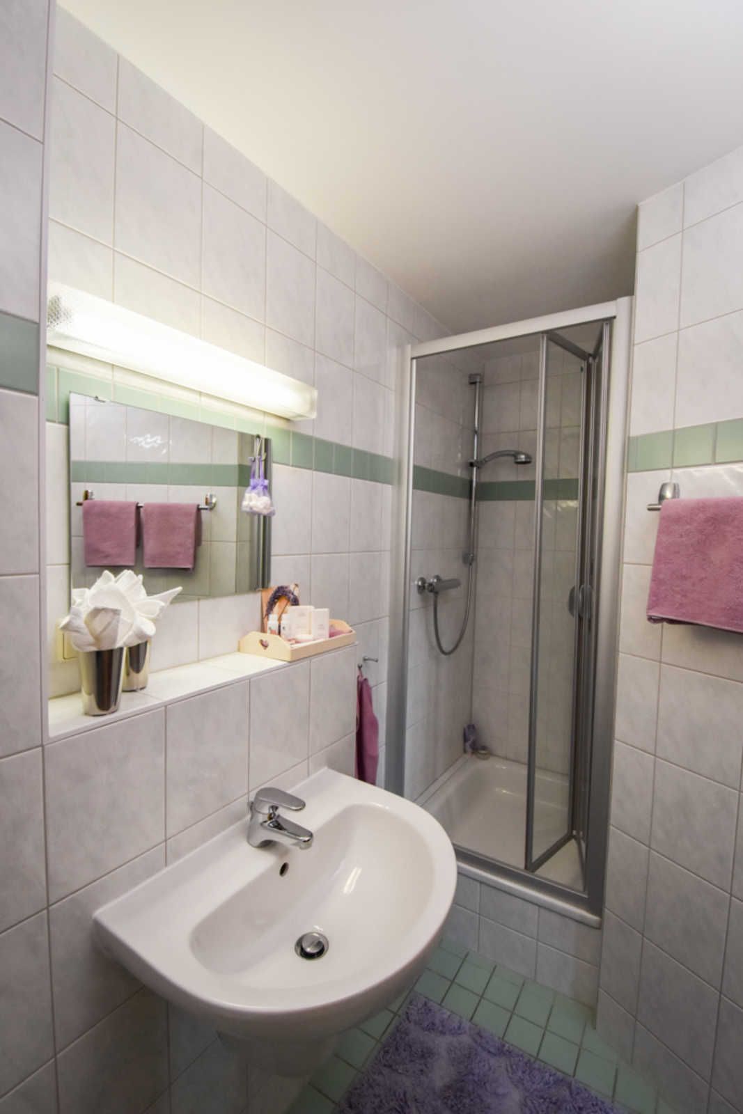 Ein Badezimmer mit Waschbecken, Spiegel, Dusche und Fliesenwänden.
