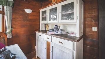A wooden interior with a white cabinet, a table with a cup and saucer, and a window with curtains.