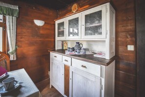 Un intérieur en bois avec un meuble blanc, une table sur laquelle se trouvent une tasse et une soucoupe, et une fenêtre avec des rideaux.