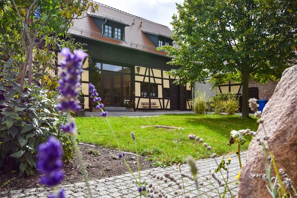 A building with a traditional half-timbered facade, a paved courtyard, and surrounding greenery.