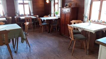 A dining area with wooden tables and chairs, a cabinet with decorative items, and windows with curtains.
