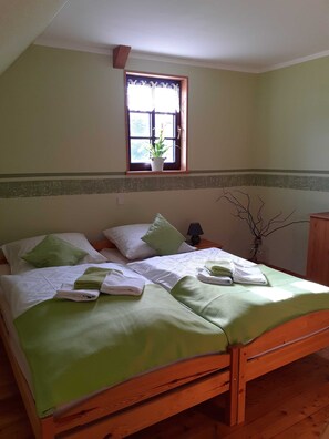 A wooden bed with green bedding, a window with a plant, and a bedside lamp.