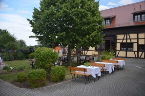 An outdoor dining area with tables and benches, surrounded by greenery and a building with a tiled roof. - EZ Gartenblick - Lavendelhof - Die Idyllische Landpension (Crimmitschau)