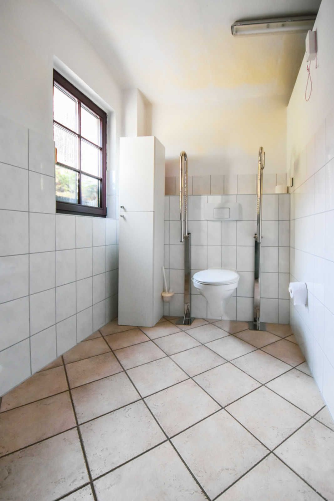 Une salle de bain avec des carreaux blancs, une fenêtre, des toilettes et un espace douche.