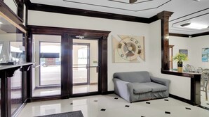 A lobby with a reception desk, a grey sofa, a clock on the wall, and a door leading outside. - Three Rivers Executive Inn & Suites By OYO (Three Rivers)