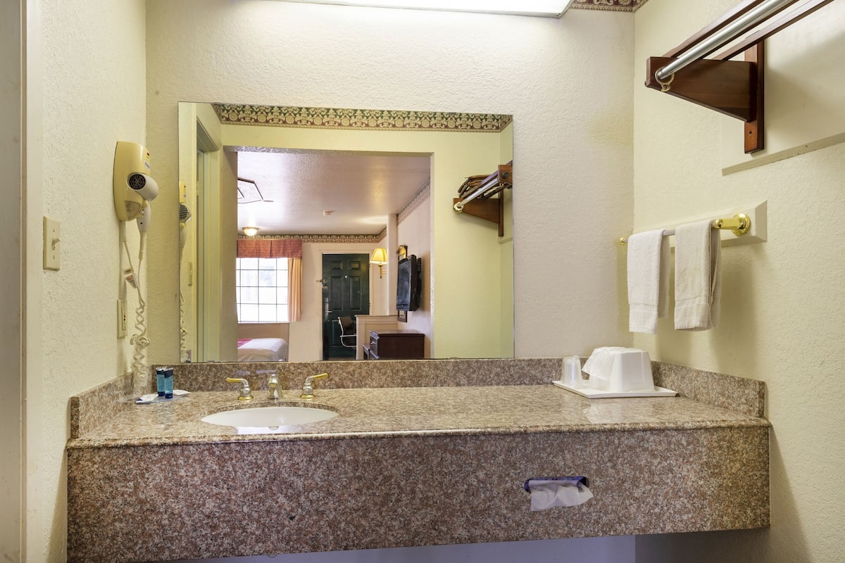 A bathroom with a granite countertop, a sink, a mirror, a hairdryer, and a towel rack.