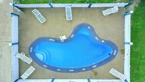 An aerial view of a swimming pool with a surrounding deck, lounge chairs, and a covered area. - Three Rivers Executive Inn & Suites By OYO (Three Rivers)