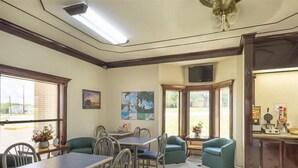 A dining area with tables and chairs, a television, and artwork on the walls. - Three Rivers Executive Inn & Suites By OYO (Three Rivers)