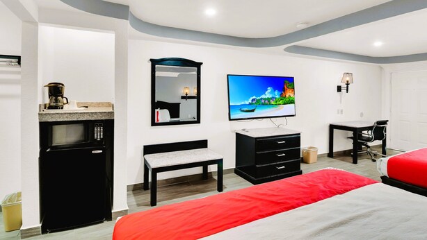 A hotel room with a bed, a TV, a desk, a chair, a microwave, a trash bin, and a mirror. - Three Rivers Executive Inn & Suites By OYO (Three Rivers)