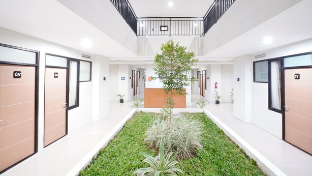 Un hall d’hôtel moderne avec un comptoir d’accueil central, un petit jardin intérieur et un escalier menant à un étage supérieur.