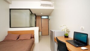 Une chambre d’hôtel avec un lit, un bureau avec un ordinateur portable, un petit réfrigérateur et une plante en pot.