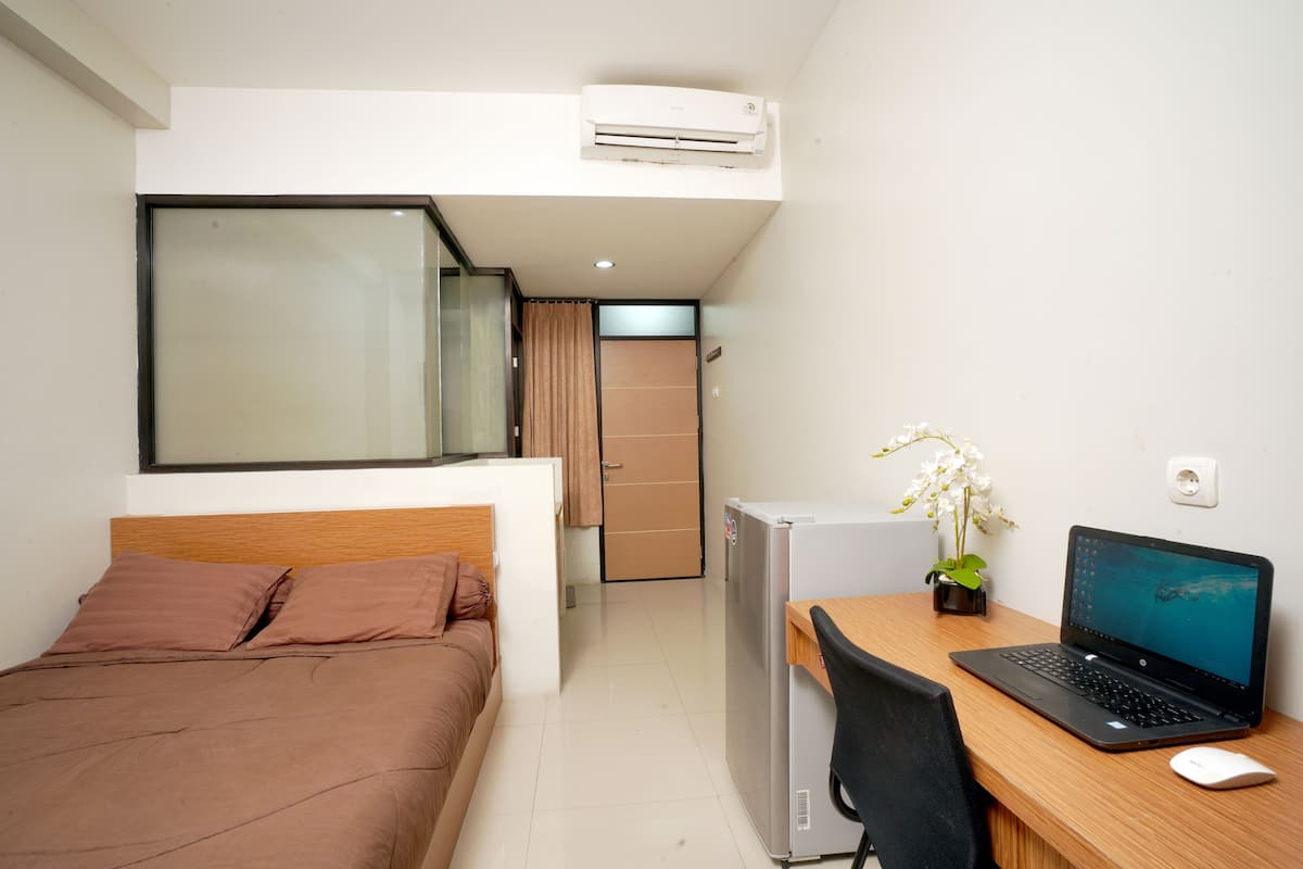 Une chambre d’hôtel avec un lit, un bureau avec un ordinateur portable, un petit réfrigérateur et une plante en pot.