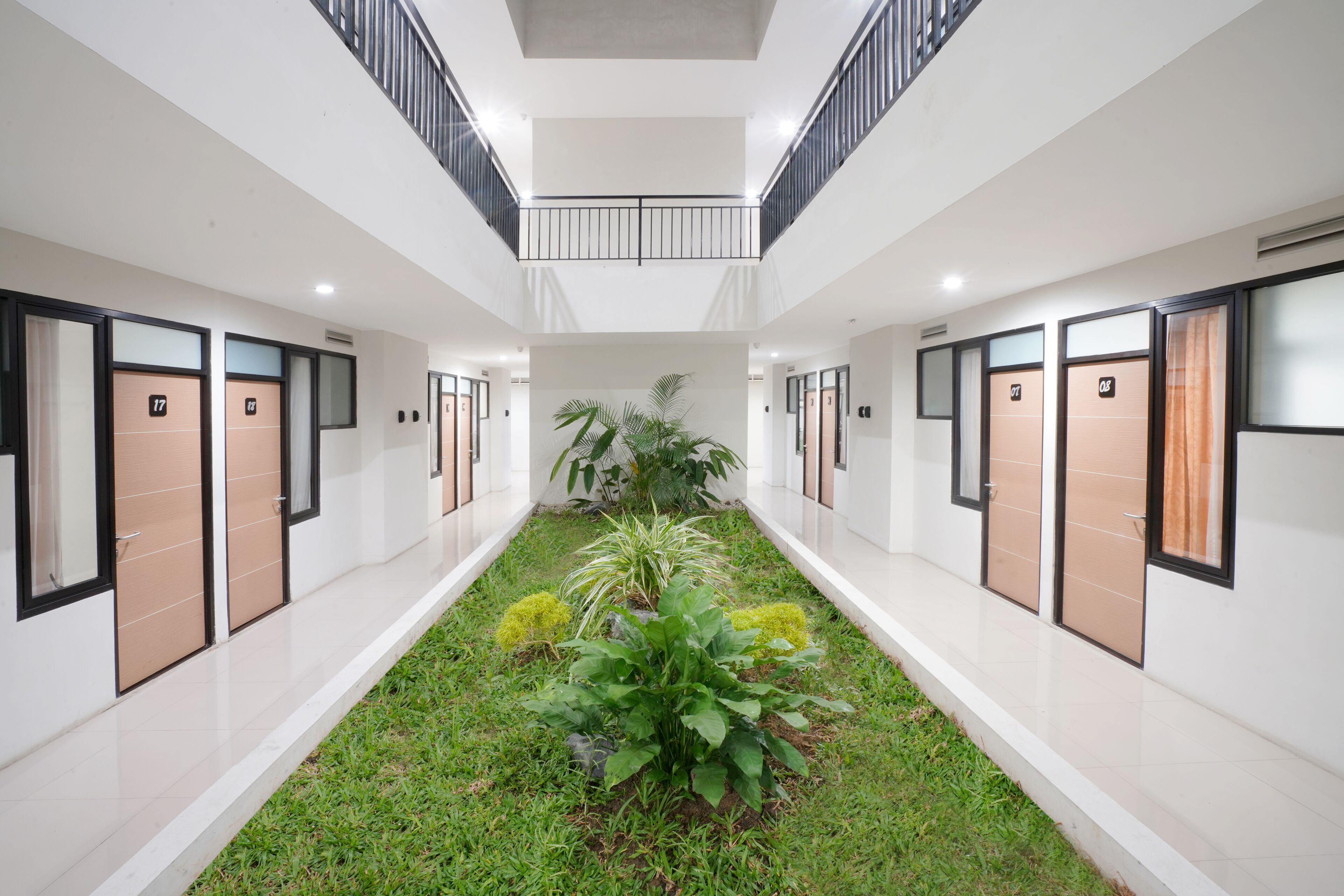 Corredor moderno de hotel com um jardim central, vários quartos de cada lado e uma varanda com vista para o jardim.