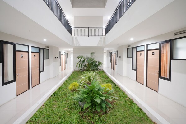 Un pasillo moderno de hotel con un jardín central, varias habitaciones a ambos lados y un balcón con vistas al jardín.
