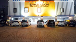 Un hôtel appelé D'Paragon, doté d’un design moderne, avec un parking pavé de briques où plusieurs voitures sont garées devant l’entrée.