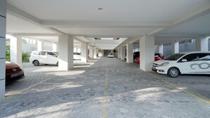 Un espace de stationnement couvert où sont garées plusieurs voitures, avec des piliers blancs et un sol carrelé.