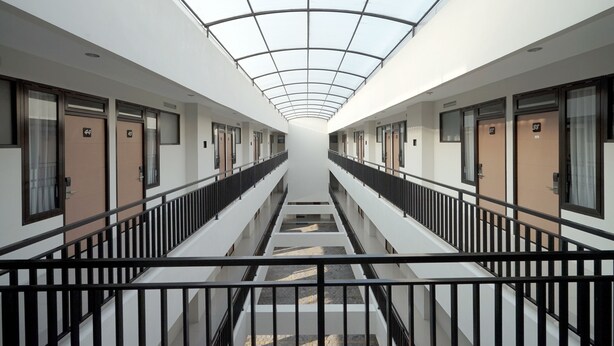 Un couloir d’hôtel moderne avec un plafond en verre, de nombreuses portes et un escalier central.