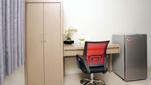 Une pièce comprenant une armoire en bois, un bureau avec une chaise, un réfrigérateur et une orchidée en pot.