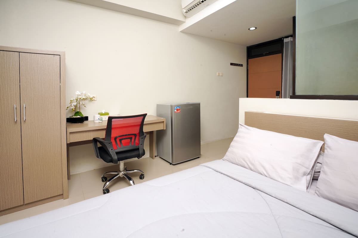 A hotel room with a bed, a desk with a chair, a refrigerator, and a wardrobe.