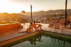 Zona de piscina con vistas a un paisaje urbano y colinas al fondo.