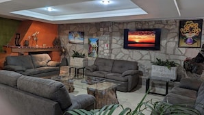 Ein modernes Wohnzimmer mit Steinwand, mehreren Sofas, einem Glastisch und verschiedenen Kunstwerken.