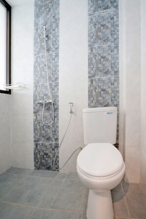 Ein Badezimmer mit gefliestem Boden, Toilette, Dusche inklusive Handbrause und einer Wand mit Mosaikfliesen.