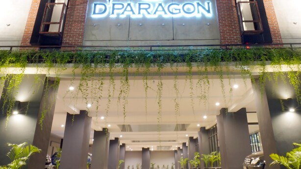 Um edifício com uma placa de destaque 'D'PARAGON', apresentando um design moderno com elementos de tijolo e concreto, e uma área de entrada coberta com plantas em vasos.