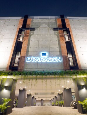 Un edificio con un llamativo letrero 'D'PARAGON', que presenta un diseño moderno con detalles de ladrillo y hormigón, y una zona de acceso cubierta con plantas en macetas.