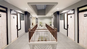 Corredor moderno de hotel com escada central, portas numeradas e plantas em vasos.