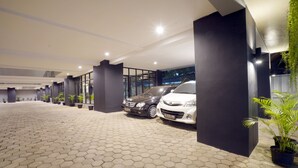 Uma área de estacionamento coberta com azulejos hexagonais, dois carros estacionados e plantas em vasos ao longo das paredes.