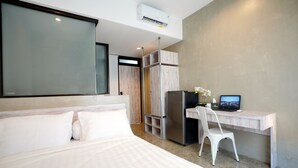 Quarto de hotel moderno com uma cama grande, uma escrivaninha com um computador e um refrigerador.