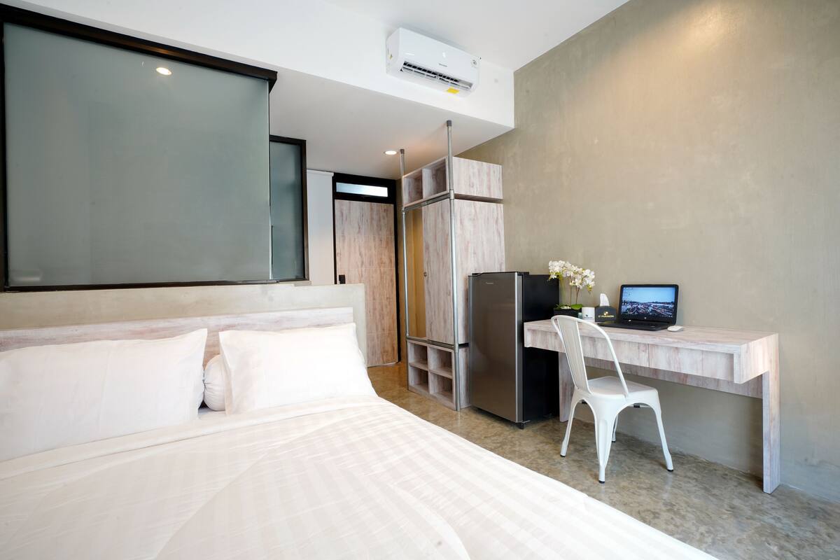 A modern hotel room with a large bed, a desk with a computer, and a refrigerator.