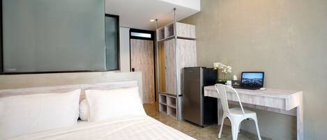 A modern hotel room with a large bed, a desk with a computer, and a refrigerator.