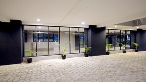 Um lobby de hotel moderno com piso de azulejos hexagonais, grandes portas de vidro e plantas em vasos.