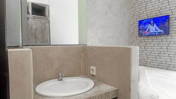 A bathroom with a sink, mirror, and a TV mounted on the wall.