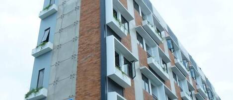 Ein mehrstöckiges Gebäude mit modernem Design, das Ziegel- und Betonfassaden sowie begrünten Balkone zeigt.