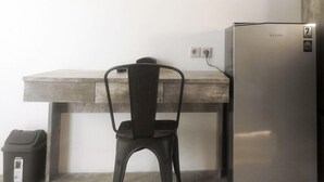 A kitchenette with a stainless steel refrigerator, a wooden countertop, a black chair, and a trash bin. - Dparagon Gajah Mada (Jakarta)