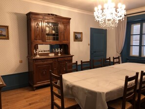 A dining room with a wooden cabinet, a chandelier, a table set for six, and a blue door. - Magnifique Appartement Style Maison de Famille (Mouthe)