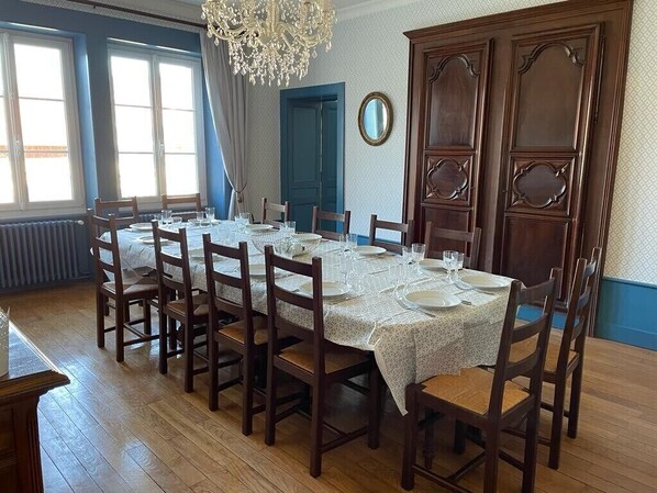A dining room with a long table set for six, wooden chairs, a chandelier, and a large wooden cabinet. - Magnifique Appartement Style Maison de Famille (Mouthe)