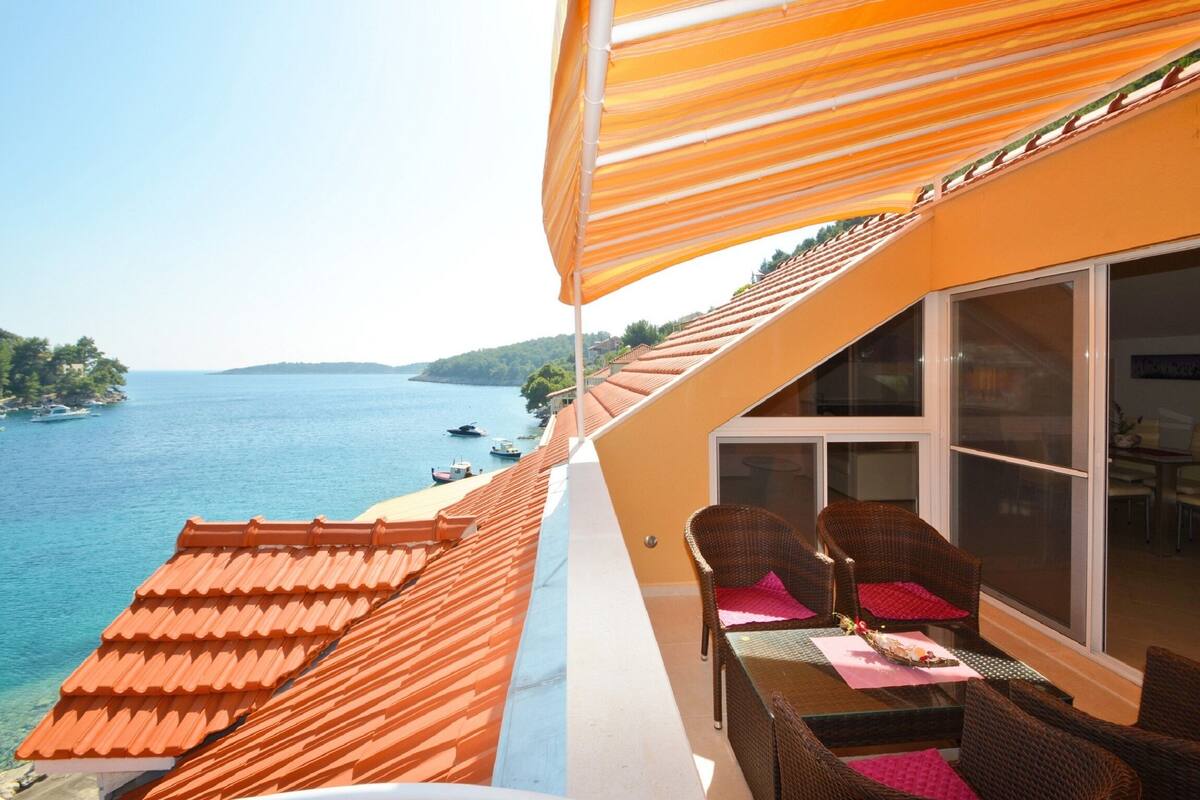 A balcony with a view of the sea, wicker furniture, and a striped awning.