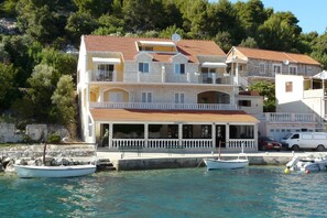A multi-story building with balconies, a restaurant, and boats docked at the waterfront. - Apartments Korcula (Blato)
