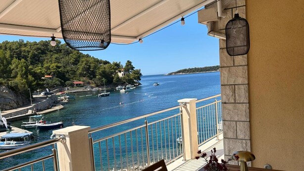 Un balcon avec vue sur la mer, les bateaux et une colline boisée.