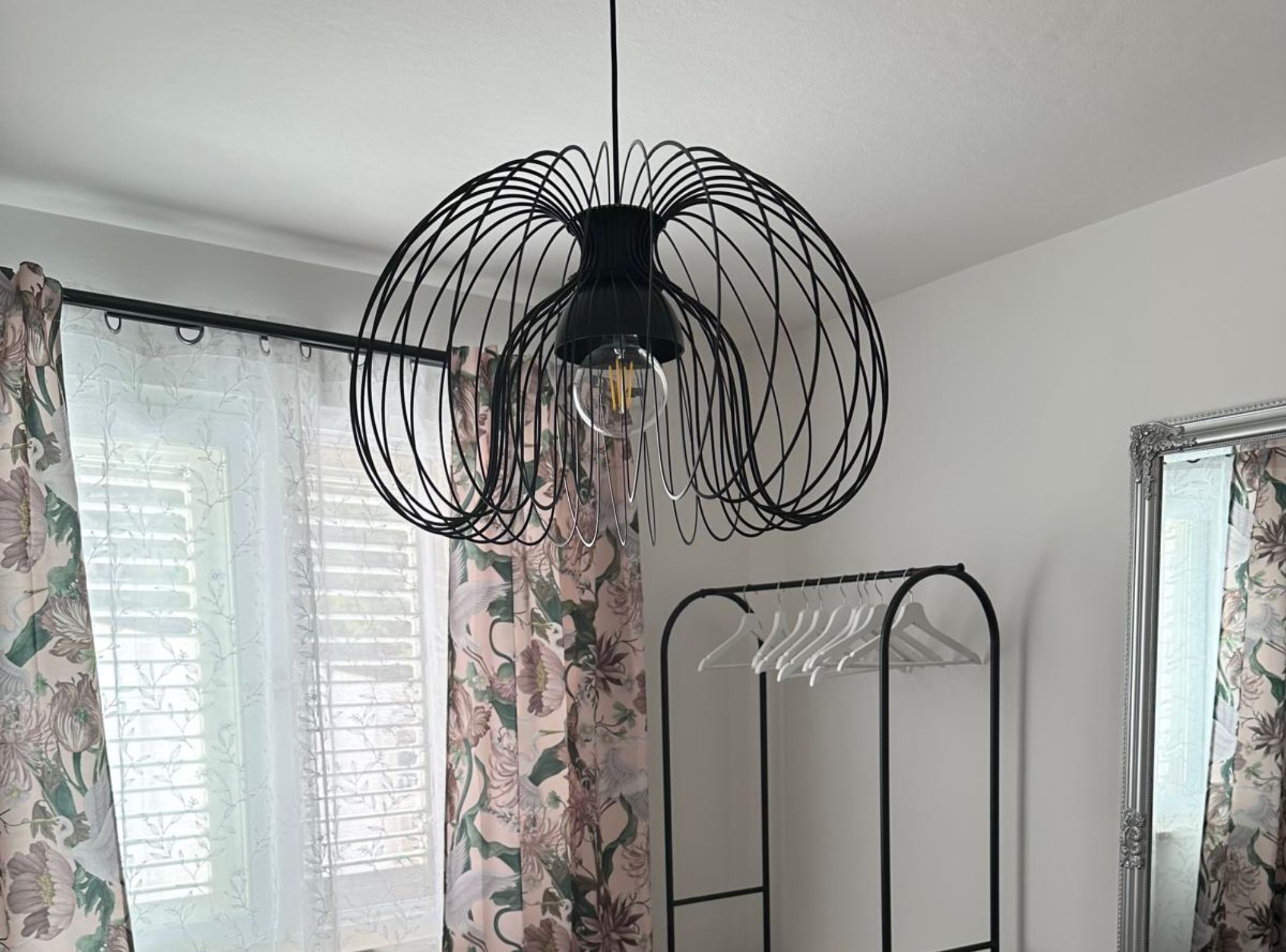 A room with a black wire chandelier, floral curtains, and a metal wardrobe.