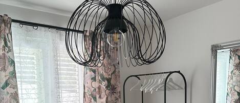 A room with a black wire chandelier, floral curtains, and a metal wardrobe.