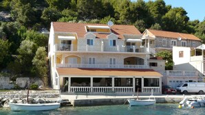 Un immeuble à plusieurs étages doté de balcons, d’un restaurant et de bateaux amarrés le long du quai.