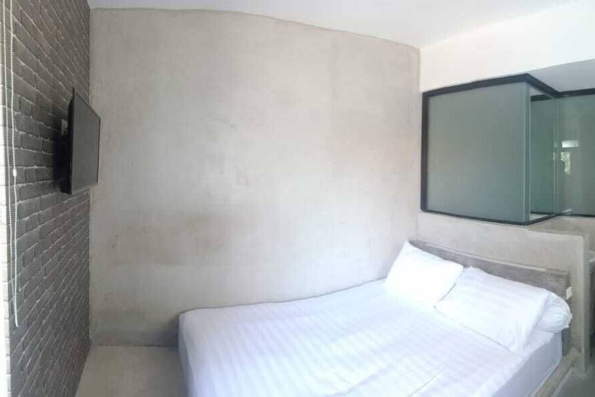 A modern hotel room with a bed, a television mounted on the wall, and a glass shower enclosure.