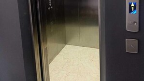 An elevator with a metallic interior, a control panel with directional buttons, and a fire alarm button on the wall. - Djuragan Kamar Gunung Anyar (Surabaya)
