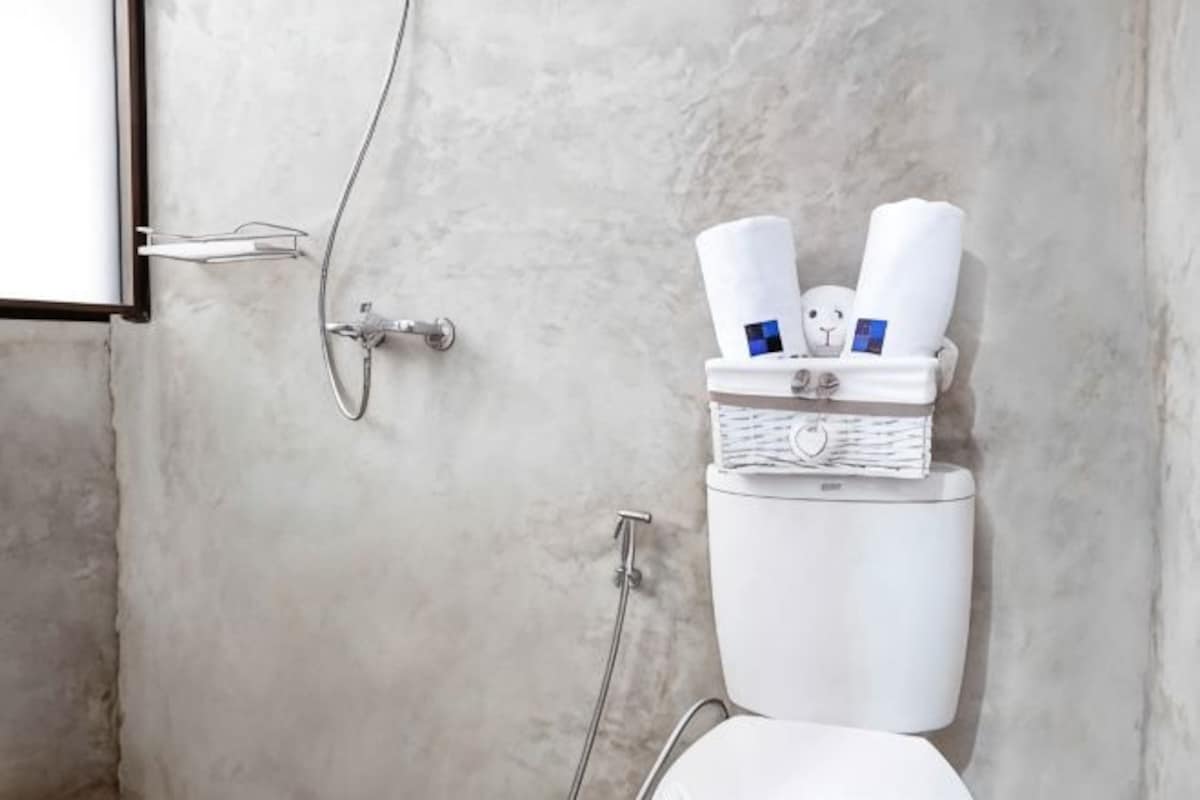 A bathroom with a white toilet, a shower, and a towel rack with towels and toiletries.