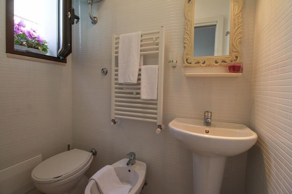 Une salle de bain comprenant des toilettes, un bidet, un lavabo, un porte-serviettes et un miroir avec un cadre décoratif.