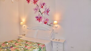 A bedroom with a bed, nightstands, a wall-mounted lamp, and a floral painting.